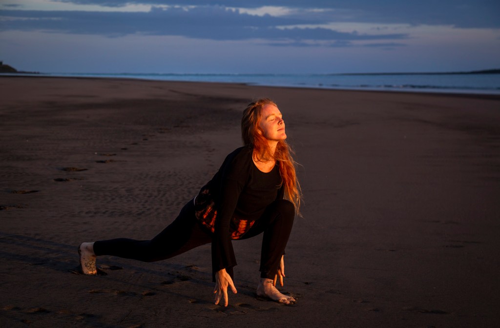 Norina yoga on the beach with ocean background in raglan new zealand